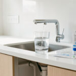 Qualité de l'eau du robinet maison : diagnostiquer et agir Cuisine lumineuse avec robinet moderne versant de l’eau claire dans un verre, kit de test domestique et plomberie discrète sous l’évier.